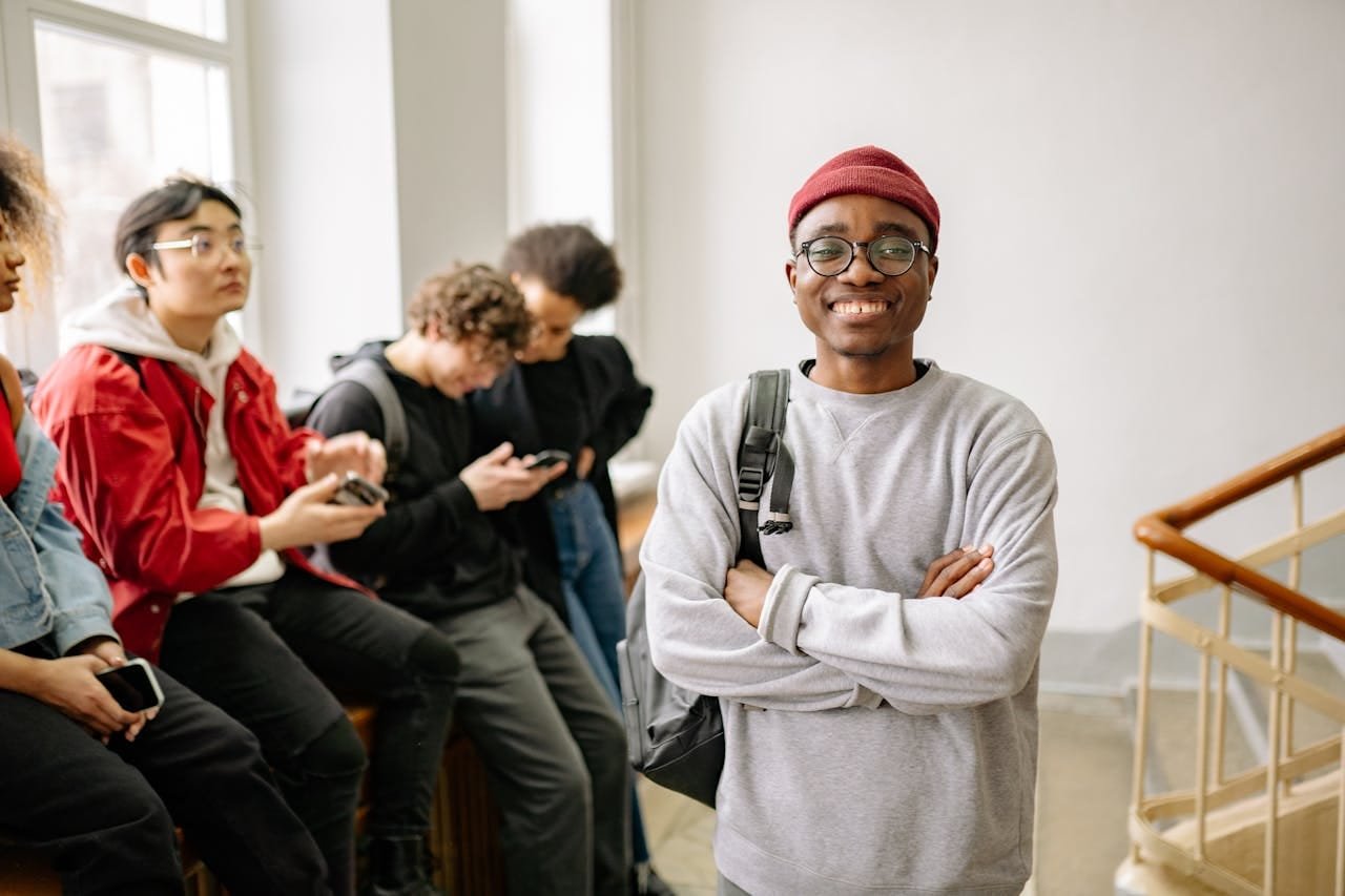 A diverse group of university students indoors, featuring a smiling young man in the foreground.